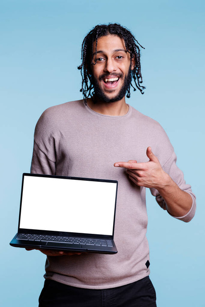Hombre árabe feliz presentación de la aplicación de software en el ordenador portátil con retrato de pantalla vacía blanca. Sonriente persona alegre señalando con el dedo a la computadora portátil y mirando a la cámara - Foto, Imagen