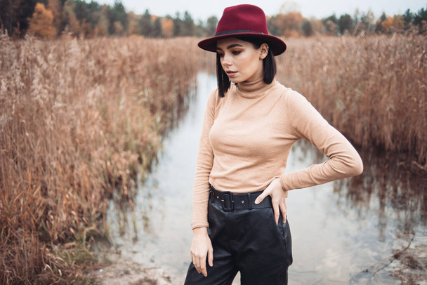 young girl in a red hat and a sweater on the background of a lake  - Фото, изображение