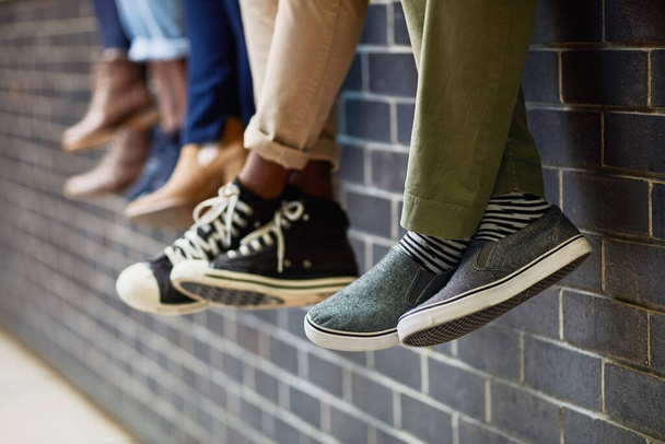Brick wall, students feet and friends outdoor on university campus together with sneakers. Relax, youth and foot at college with people legs ready for education, study and urban shoes while sitting. - Photo, Image