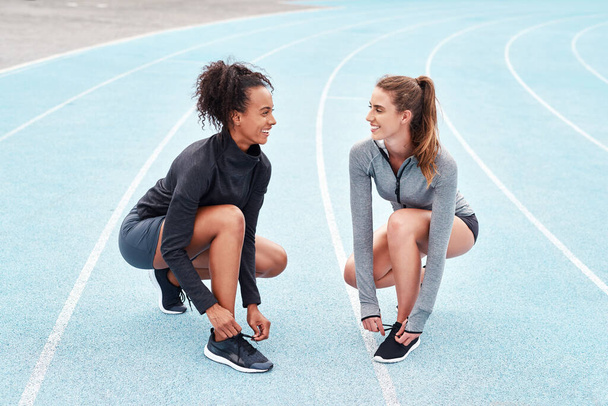 Teamwork is the best motivation. Full length shot of two attractive young athletes crouching together and tying their shoelaces before running on a track - Photo, Image