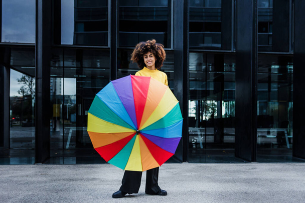 jeune femme afro-américaine homosexuelle avec drapeau arc-en-ciel ou parapluie dans la ville d'Amérique latine, hispanique et caribéenne LGBT femelle aux cheveux afro  - Photo, image