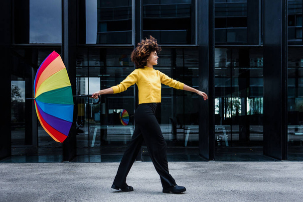 junge Afroamerikanerin Homosexuelle mit Regenbogenfahne oder Regenschirm tanzen und feiern Stolz Monat in der Stadt von Lateinamerika, hispanische und karibische LGBT-Frau mit Afro-Haaren - Foto, Bild