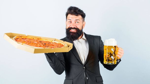 Pizzan aika. Parrakas mies, jolla on maukasta pizzaa ja olutmuki. Tyytyväinen mies herkullisella pizzalla ja kylmällä oluella. Pikaruokaa. Italialaista ruokaa. Työlounas. Hymyilevä liikemies pizzan ja oluen kanssa. Pizzeria - Valokuva, kuva