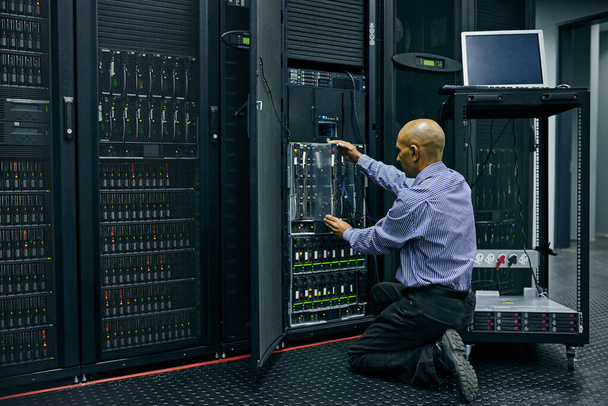 Database, software and a man engineer in a server room for cybersecurity maintenance on storage hardware. Computer network or mainframe with a technician working on information technology equipment. - Photo, Image