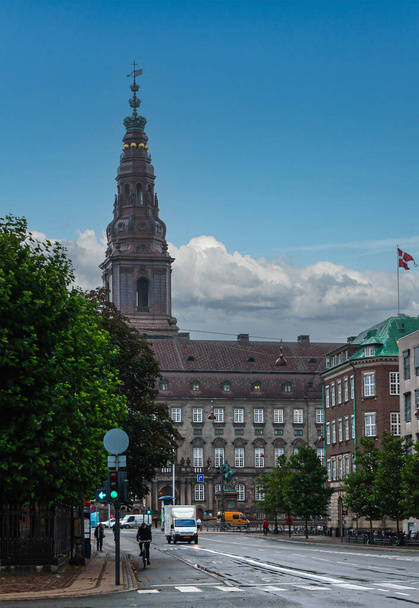 Copenhagen, Denmark - September 14, 2010: Christiansborg Slot tower and facade with King Frederik VII statue seen from Holmenscanal street under blue cloudscape. Green foliage and traffic - Foto, imagen