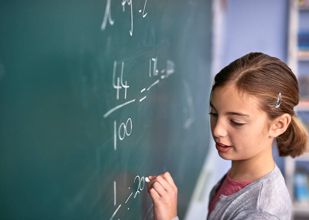 Shes almost got it. an elementary school girl writing on a blackboard in class - Foto, imagen