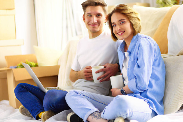 Couple buying online with a laptop and moving house sitting on the floor. - Valokuva, kuva