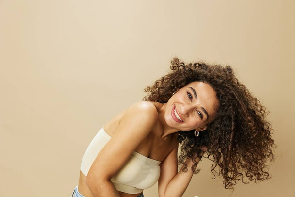 Woman dries curly hair with blow dryer, home beats styling products, smile on beige background. High quality photo - Photo, Image