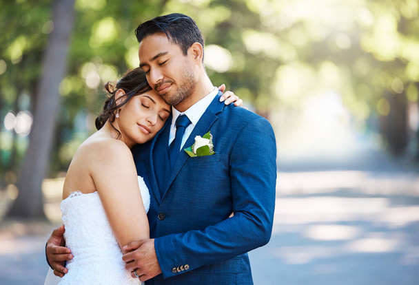 Beautiful bride leaning on grooms shoulder while standing outside. Loving newlywed couple enjoying romantic moments together. Feeling safe and secure. - Photo, Image