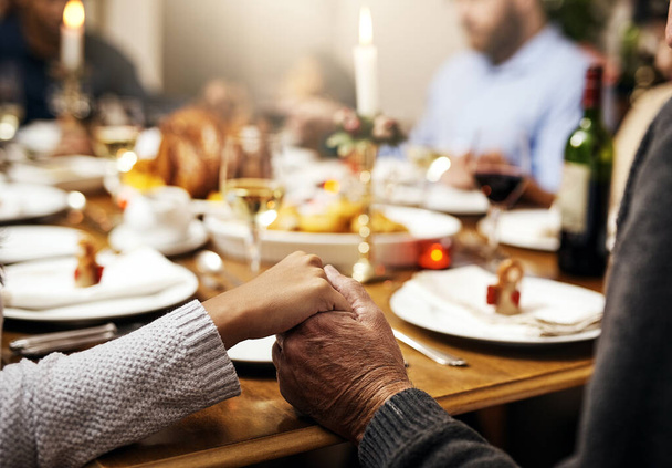 Close-up, ação de graças e mão segurando com a família à mesa na sala de jantar para férias, comida ou adoração. Celebração, apoio e gratidão com as pessoas que rezam em casa por bondade, jantar e amor. - Foto, Imagem