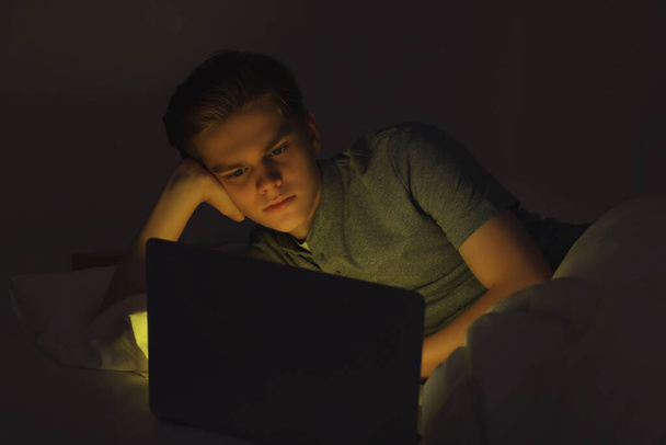 Teenage boy using laptop on bed at night. Internet addiction - Fotó, kép
