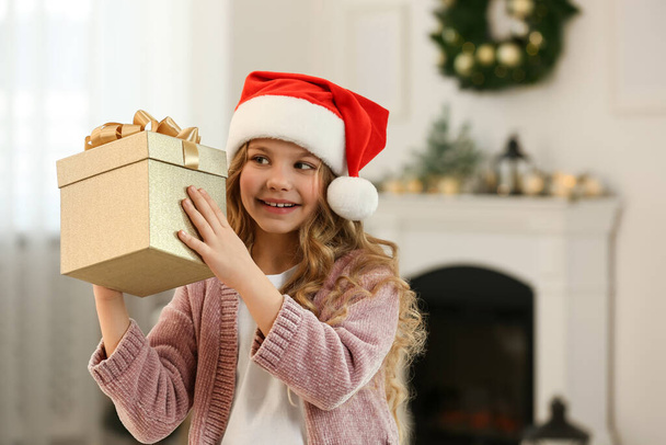 Happy little girl with Christmas gift near fireplace at home. Space for text - Φωτογραφία, εικόνα
