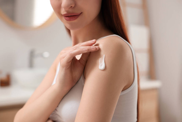 Young woman applying body cream onto shoulder in bathroom, closeup - Fotografie, Obrázek