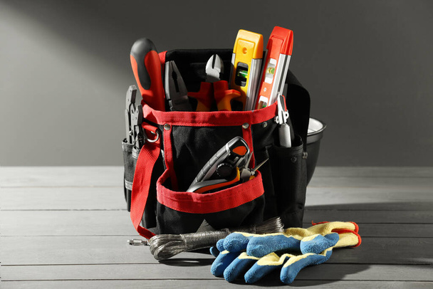 Bag with different tools for repair and protective gloves on wooden table - Fotó, kép