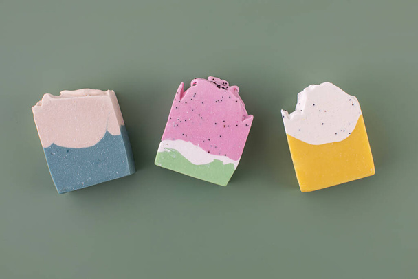 Pieces of different shapes and colors of handmade soap on a green background. The concept of natural cosmetics, hygiene. - Zdjęcie, obraz