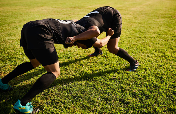 Using our legs to overthrow each other. Full length shot of two unrecognizable sportsmen tacking each other during a rugby game during the day - Fotografie, Obrázek