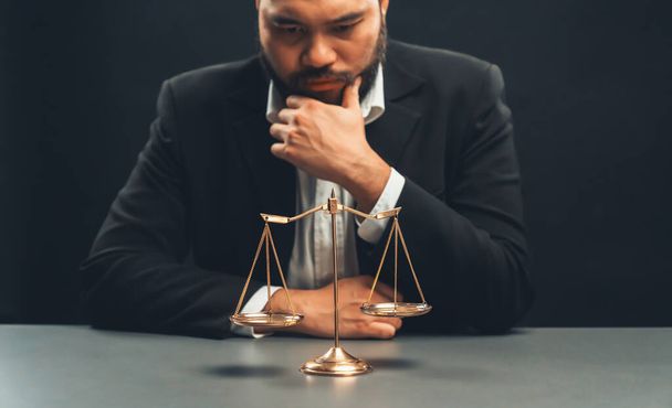 Focus scale balance with blur lawyer sitting at his desk with worried and exhausted expression, feeling weight of pressure and stress of making hard decision on verdict. equility - 写真・画像