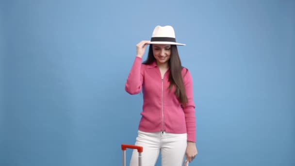 Vrouw in casual kleding en witte hoed met paspoort en rode koffer geïsoleerd op blauwe achtergrond. Reizigers reizen in het buitenland weekend weg. Vliegreis concept. - Video