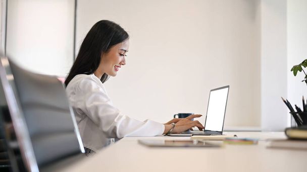 Vista laterale immagine di una giovane attraente donna d'affari asiatica o impiegata donna che utilizza il suo computer portatile in una sala riunioni. - Foto, immagini