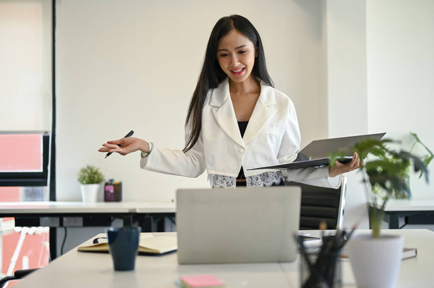 Очаровательная молодая азиатская ассистентка или деловая женщина просматривает деловые документы на папке и работает над своим проектом в своем офисе. - Фото, изображение