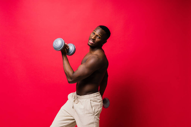 Portrait of happy african man with dumbbells over red and black background - Foto, Bild