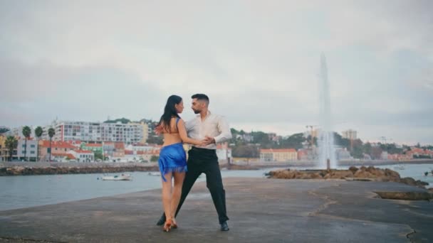 悲観的な堤防でラテンアメリカのダンスを行う情熱的なペア.プロのダンサーが海岸前の街で魅惑的に動きます。官能的なカップル出演ダンスルンバでウォーターフロントでスローモーション - 映像、動画