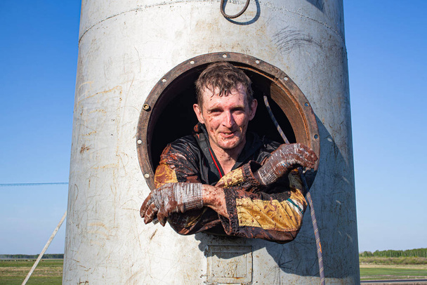 ein arbeitender Industriekletterer, der beim Streichen eines Wasserturms eine Rauchpause einlegt. Schwierige Arbeit in einem geschlossenen Raum - Foto, Bild