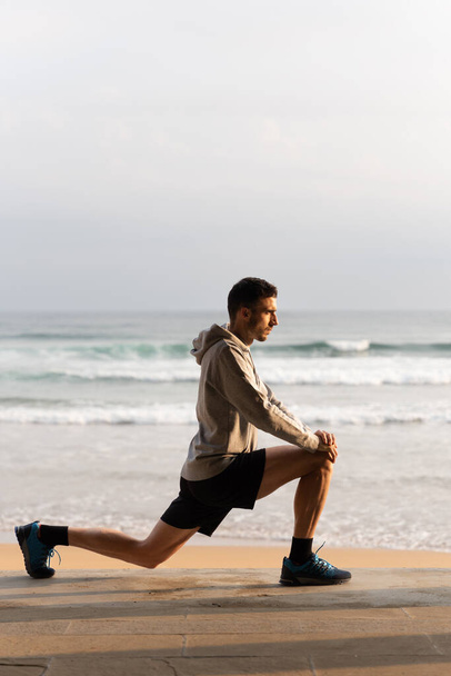 Young sportsman stretching legs outdoors before training at sunrise - Photo, Image