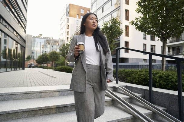 Business Chinese woman walking in the city and holding a cup of coffee - Photo, Image