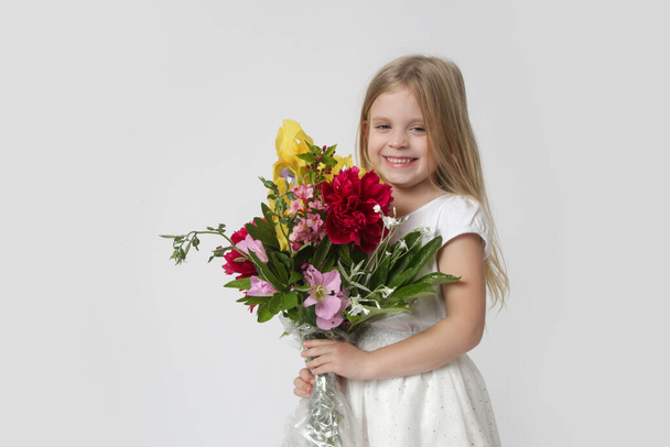 Studio portrait of beautiful little girl holding big colorful bouquet of various flowers. - 写真・画像