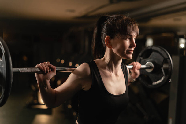 Mujer de fitness haciendo ejercicio con barra de peso pesado en el gimnasio. Mujer poniendo esfuerzo mientras hace ejercicio con pesas pesadas. Copiar espacio - Foto, Imagen