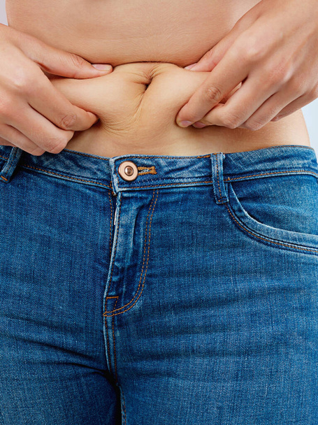 Una libra a la vez. una joven irreconocible pellizcando un rollo de grasa en su estómago en el estudio - Foto, imagen