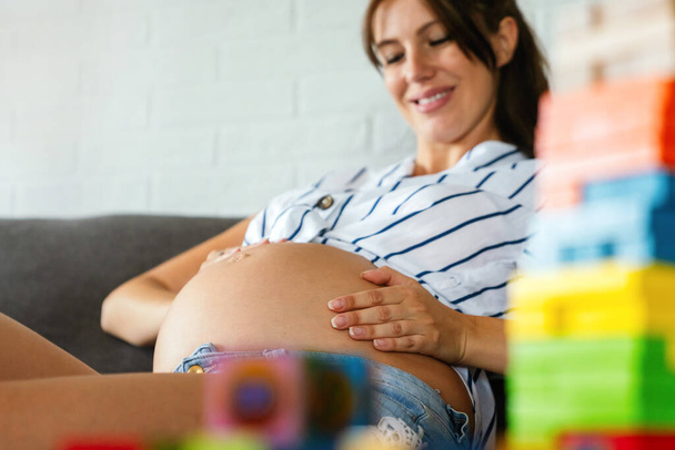 Pregnancy, rest, people and expectation concept. Happy beautiful pregnant woman touching her belly at home - Φωτογραφία, εικόνα