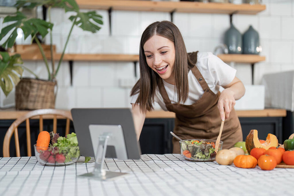 Image of young pretty lady in kitchen and cooking the salad. Looking at tablet computer. - Foto, Imagem