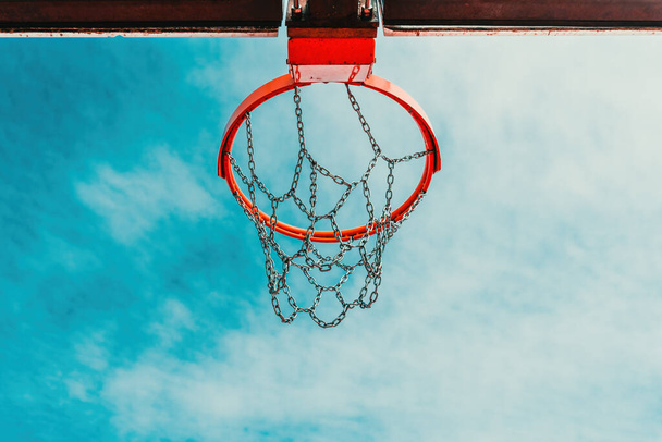 Low-angle view of an outdoor basketball hoop with a chain net against summer sky - Foto, afbeelding