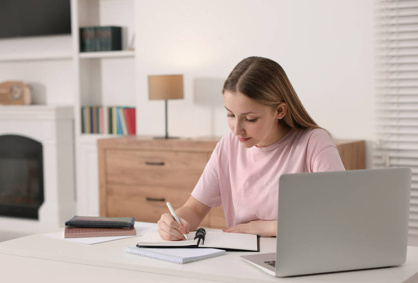 Online learning. Teenage girl writing in notepad near laptop at table - Фото, зображення