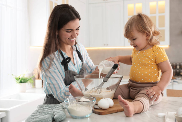 Mother and her little daughter cooking dough together in kitchen - Foto, Bild