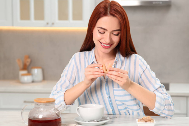 Femme heureuse avec des cheveux teints en rouge tenant biscuit fortune dans la cuisine - Photo, image