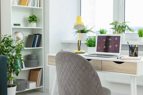 Cozy workspace with modern laptop on white wooden desk and comfortable chair at home - Photo, image
