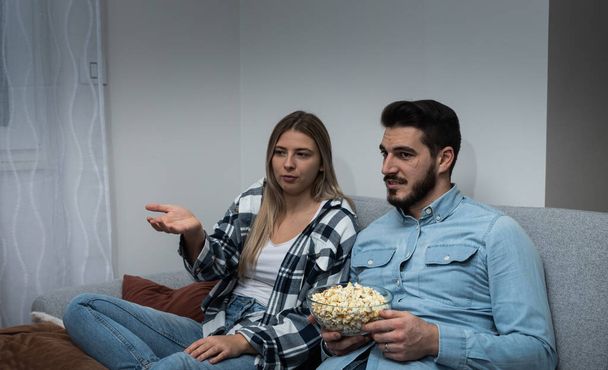 Watching TV at home. Loving couple resting on sofa and eating popcorn while enjoying movie or film on television - Foto, Imagem