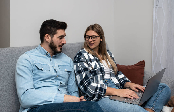 Young happy lovely couple planning budget together at home, writing notes to laptop computer, creating checklist for shopping or guest list for wedding invitations, counting chairs on ceremony - Φωτογραφία, εικόνα