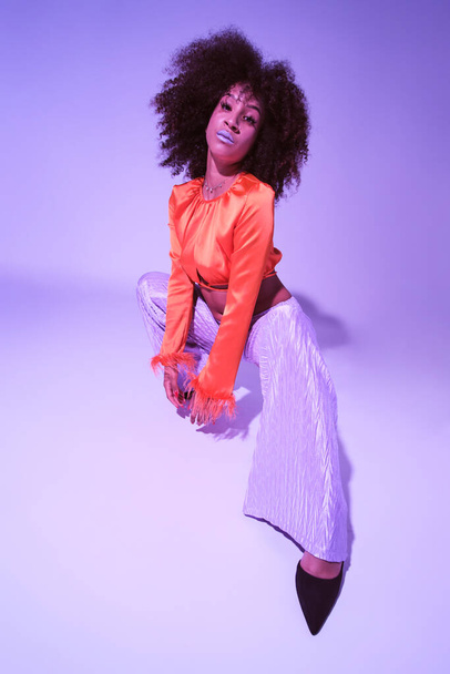 Latin girl with curly hair and colorful clothes smiling and looking at camera touching her hair while dancing - Foto, afbeelding