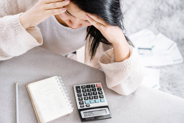 depressed Asian woman worried about her expenses calculating on calculator with list of debt writing on notebook - Valokuva, kuva