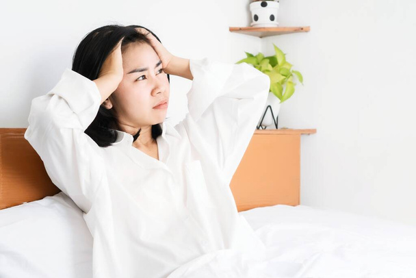 Asiatin, die ein Problem mit Depressionen hat, sitzt im Bett und hält ihren Kopf, überdenkt und fühlt sich schlecht - Foto, Bild