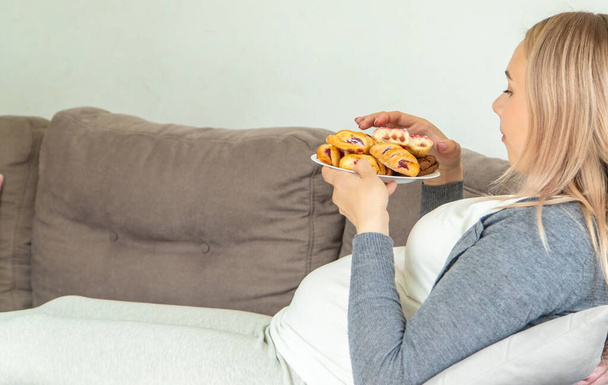 Μια έγκυος γυναίκα τρώει ένα γλυκό ντόνατ. Επιλεκτική εστίαση. Τρόφιμα. - Φωτογραφία, εικόνα