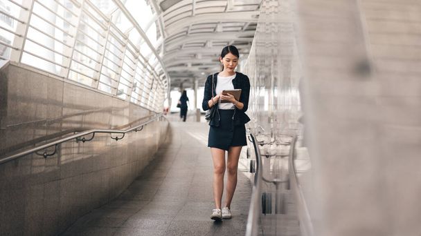 Fiatal felnőtt üzleti dolgozó ázsiai nő használja digitális tabletta az online alkalmazás tőzsde. Sétáló életmód modern technológiával. Háttér másolási hellyel a napon. - Fotó, kép