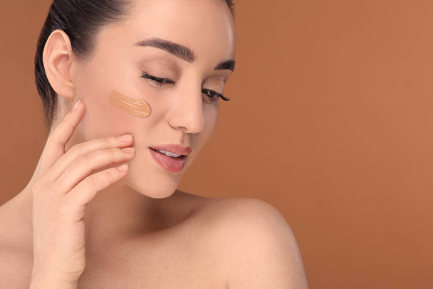 Woman with swatch of foundation on face against brown background. Space for text - Foto, Imagem