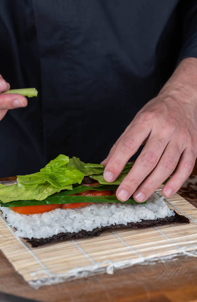 Lähikuva sushi kokki kädet valmistaa japanilaista ruokaa. Mies laittaa sushia ravintolassa. Perinteiset Aasian äyriäiset rullina leikkuulauta. - Valokuva, kuva