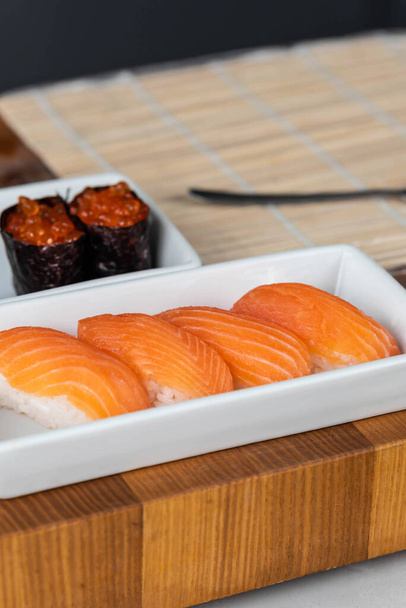 Primo piano di mani di sushi chef che preparano cibo giapponese. Uomo che cucina sushi con caviale rosso e salmone al ristorante. tradizionale asiatico frutti di mare rotoli su tagliere. - Foto, immagini