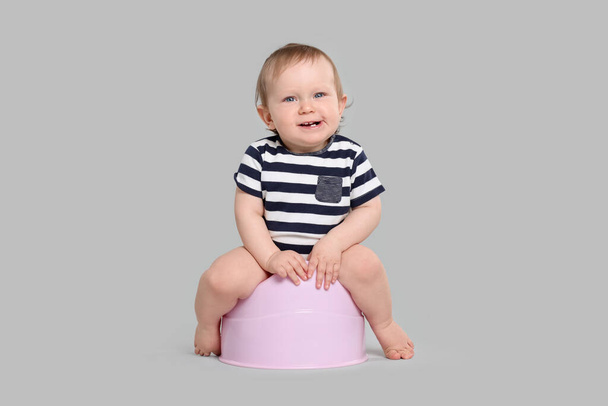 Little child sitting on baby potty against light grey background - Фото, изображение